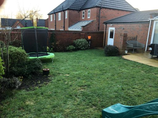 A garden with a trampoline, grassy area, a small patio, and nearby houses.